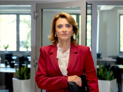 Kobieta w bordowym żakiecie na tle korytarza w biurowcu